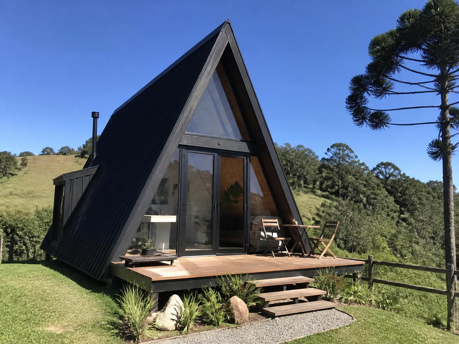 Chalé modular A-Frame Abrigo Chalet 32 com deck de madeira em terreno verde